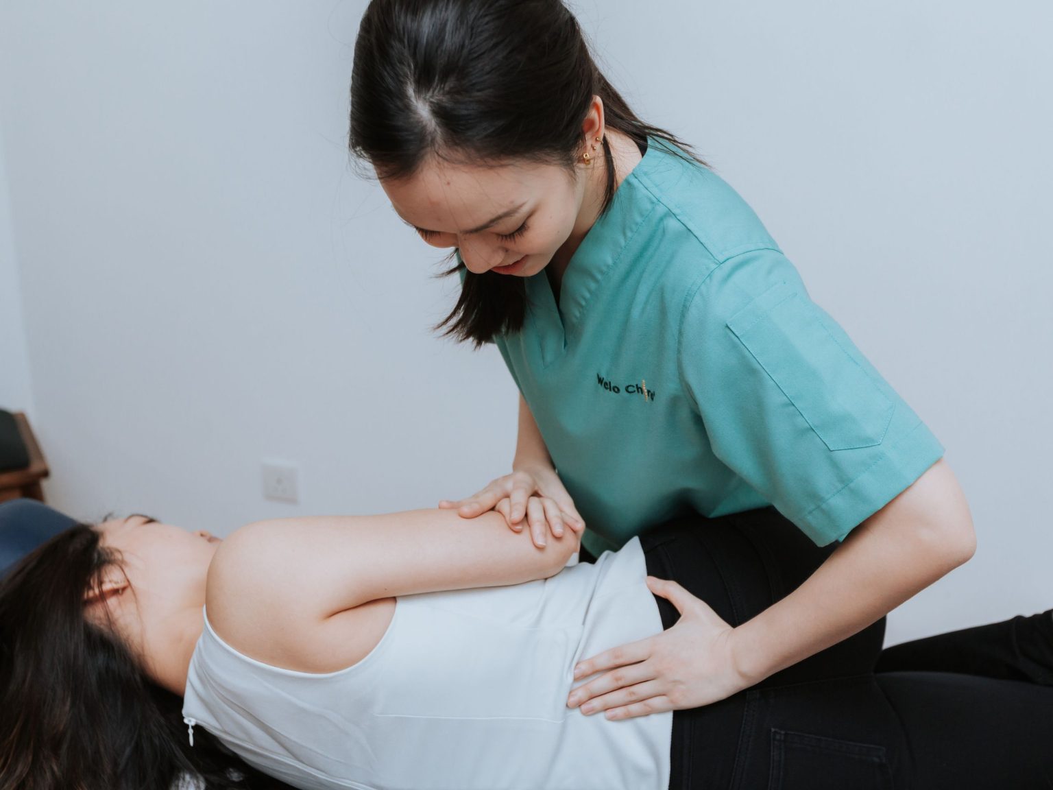 A Welo practitioner adjusting a woman's shoulder against a dark green wall